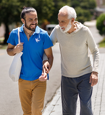 A male senior home care provider helps an elderly man with his groceries.