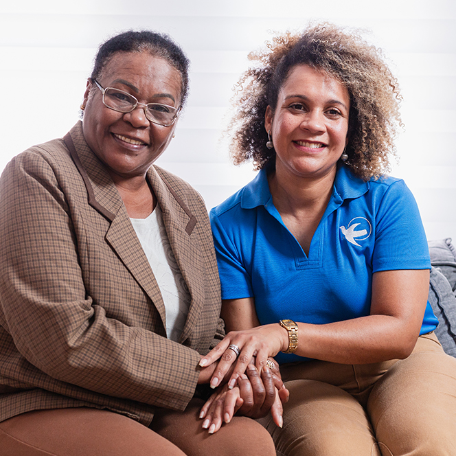 A female Visiting Angels caregiver sits with an elderly woman.